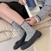 Pair of gray socks with small dark motifs and navy scalloped cuffs, worn with loafers