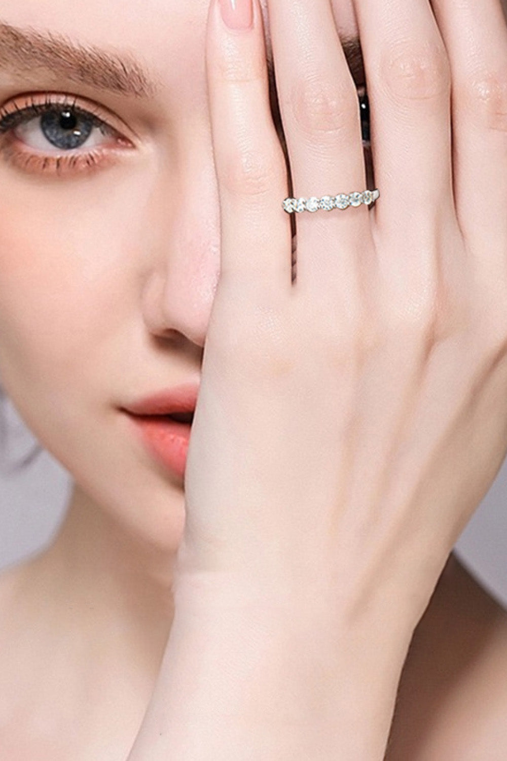 Silver-tone ring with clear stones shown on a model's hand beside her face