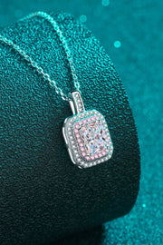 Pink-bordered rectangular pendant necklace draped over a teal cushion