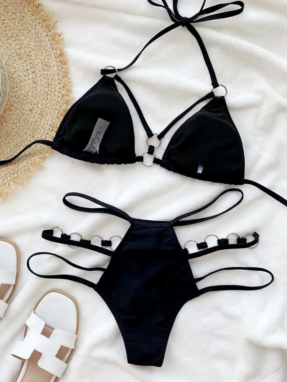 Black cutout halter bikini set laid flat on white fabric with sandals