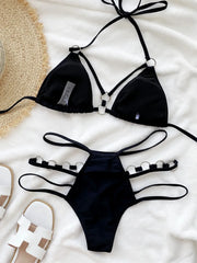 Black cutout halter bikini set laid flat on white fabric with sandals