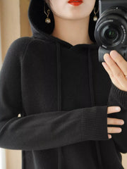 Black hooded knit sweater shown in a front mirror photo with one hand across the chest.