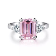 Front view of pink emerald-cut center stone ring with clear side stones
