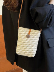 Woven crossbody bag worn over a dark jacket, showing the button-loop closure