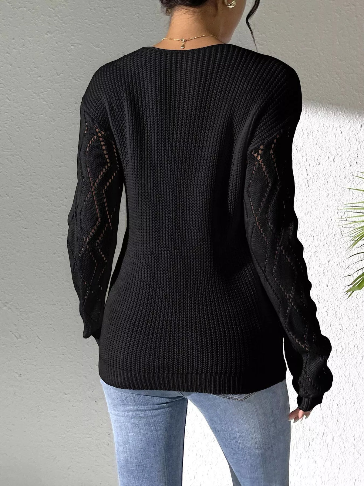 Back view of the black sweater with plain knit body and diamond-pattern sleeves.