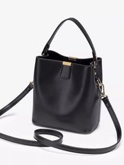 Three-quarter view of the black bucket bag with its long strap laid out beside it.