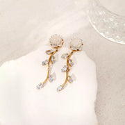 Gold-tone flower drop earrings arranged on white fabric beside a glass dish