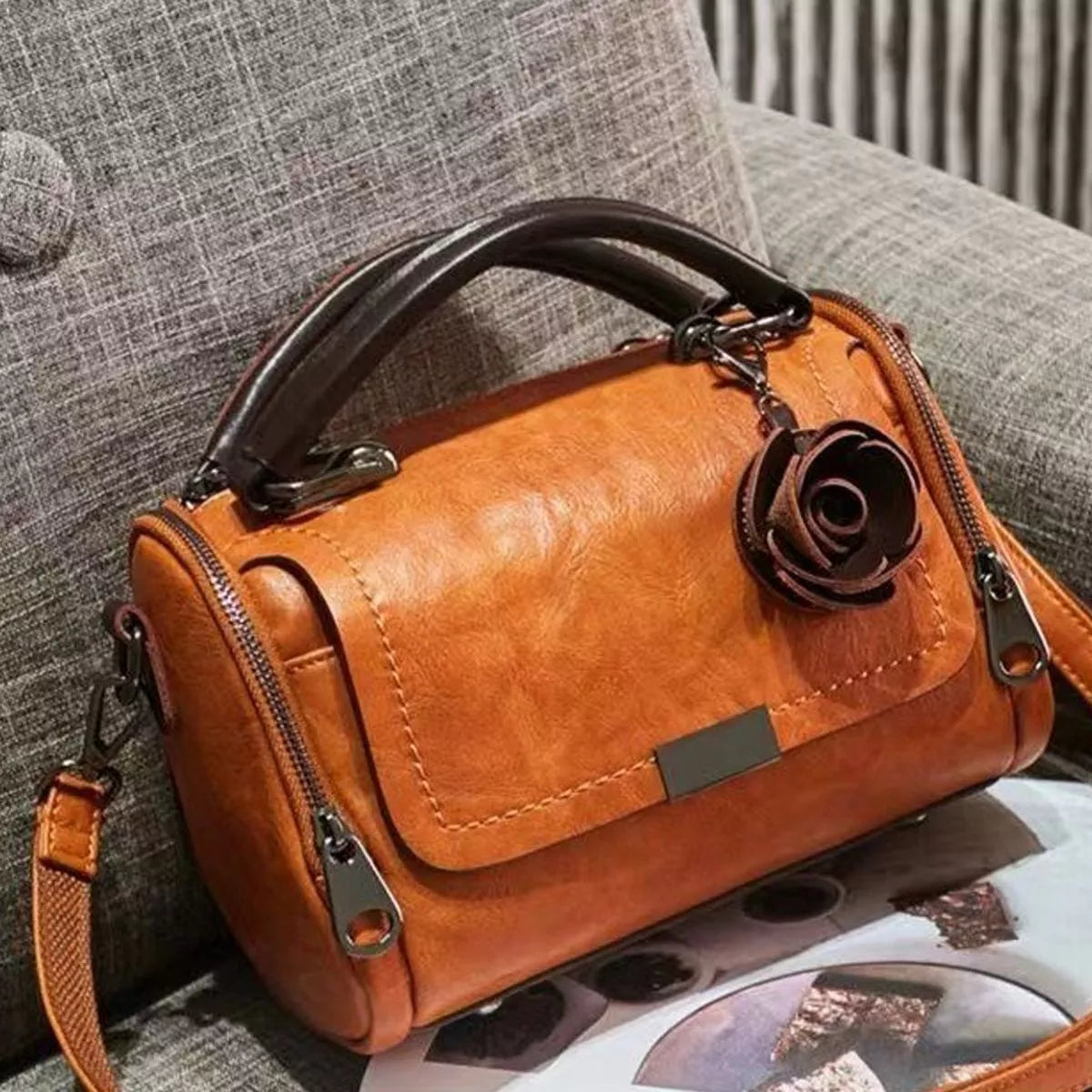 Tan flap crossbody bag with flower ornament resting at an angle on a sofa