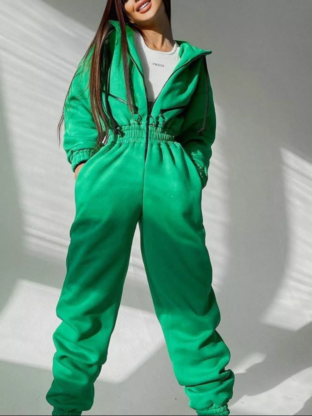 Women's green hooded jumpsuit, model front view with hands at waist