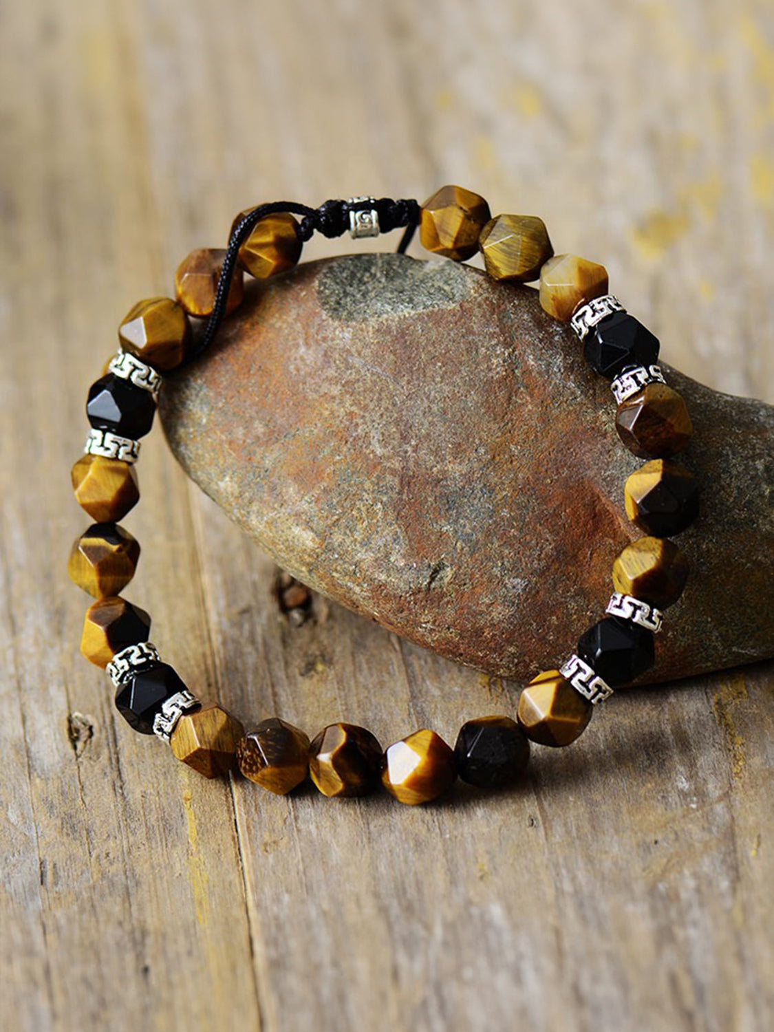 Brown and black faceted stone bracelet arranged around a rock on a wooden surface