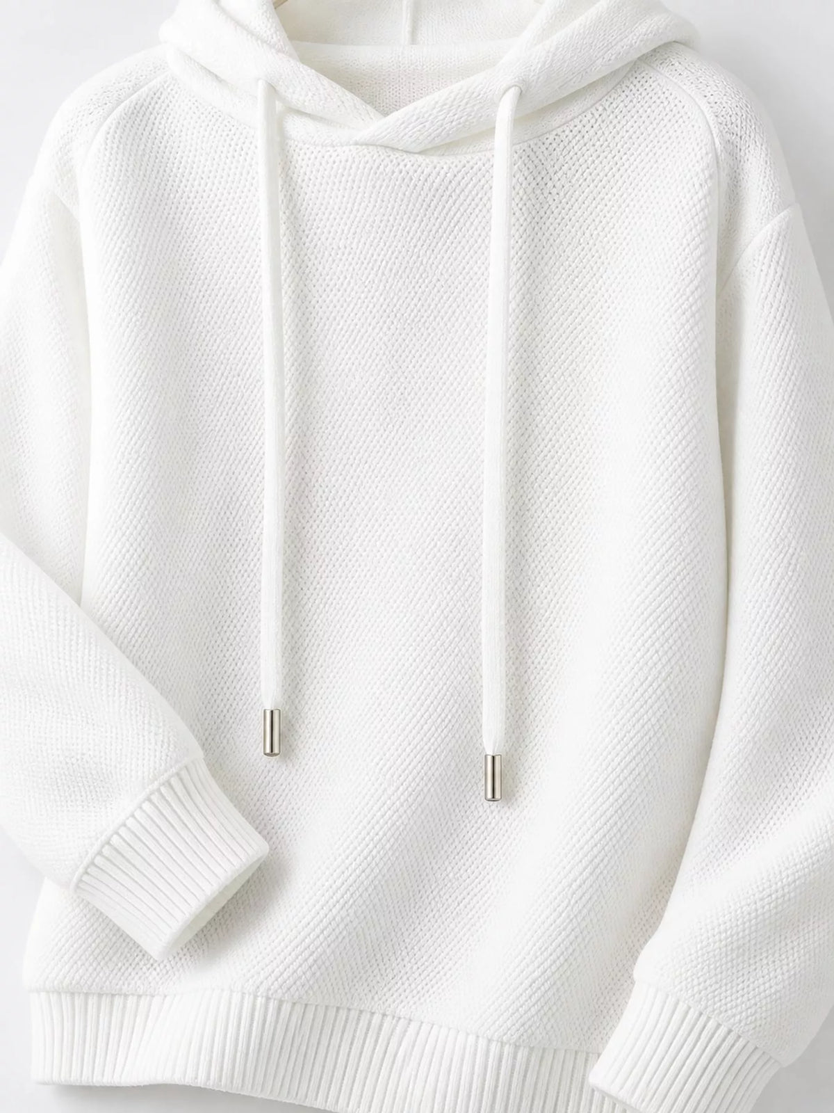 White sweater close-up showing metal-tipped drawstrings, textured knit and ribbed cuffs.