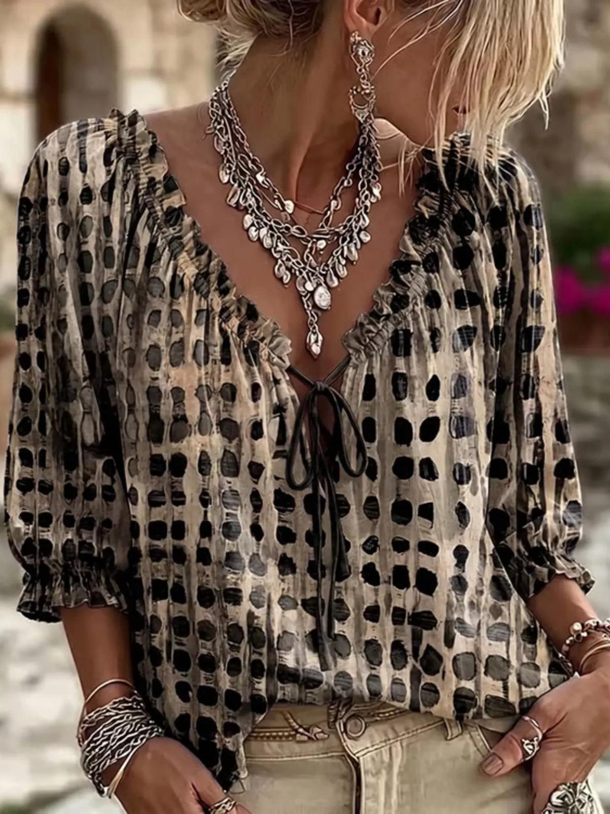Model wearing the blouse in beige with black spots and a dark tie at the neckline