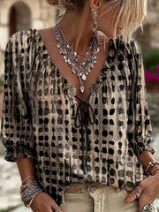 Model wearing the blouse in beige with black spots and a dark tie at the neckline