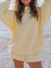 Model in a pale yellow sweatshirt and matching shorts with both arms lifted.