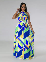 Model wearing a blue, lime and white geometric halter maxi dress, lifting one edge of the skirt.
