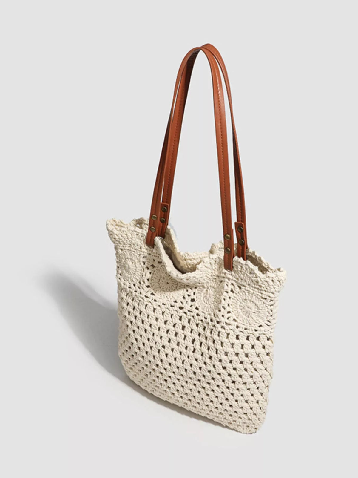 Angled view of the crochet tote showing its brown shoulder handles and open-knit side.