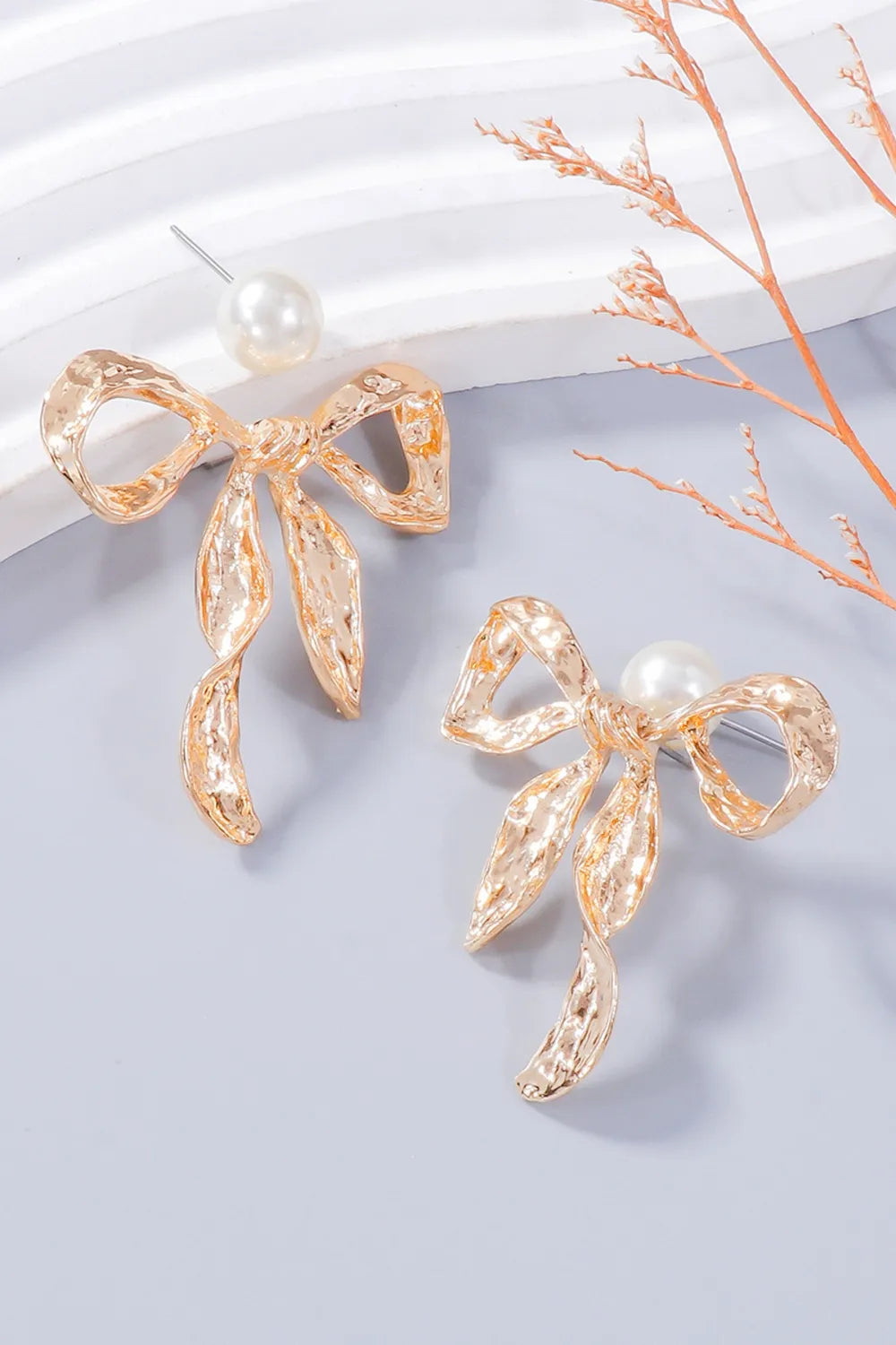 Angled close-up of gold-tone bow earrings with white bead tops