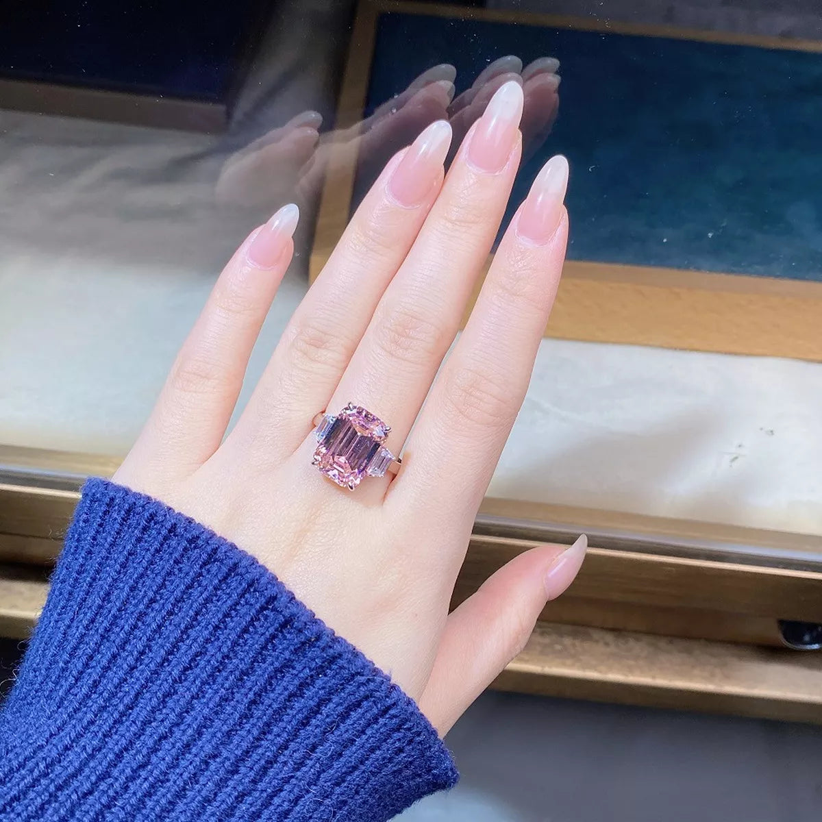 Pink rectangular gemstone ring with clear side accents shown on a hand