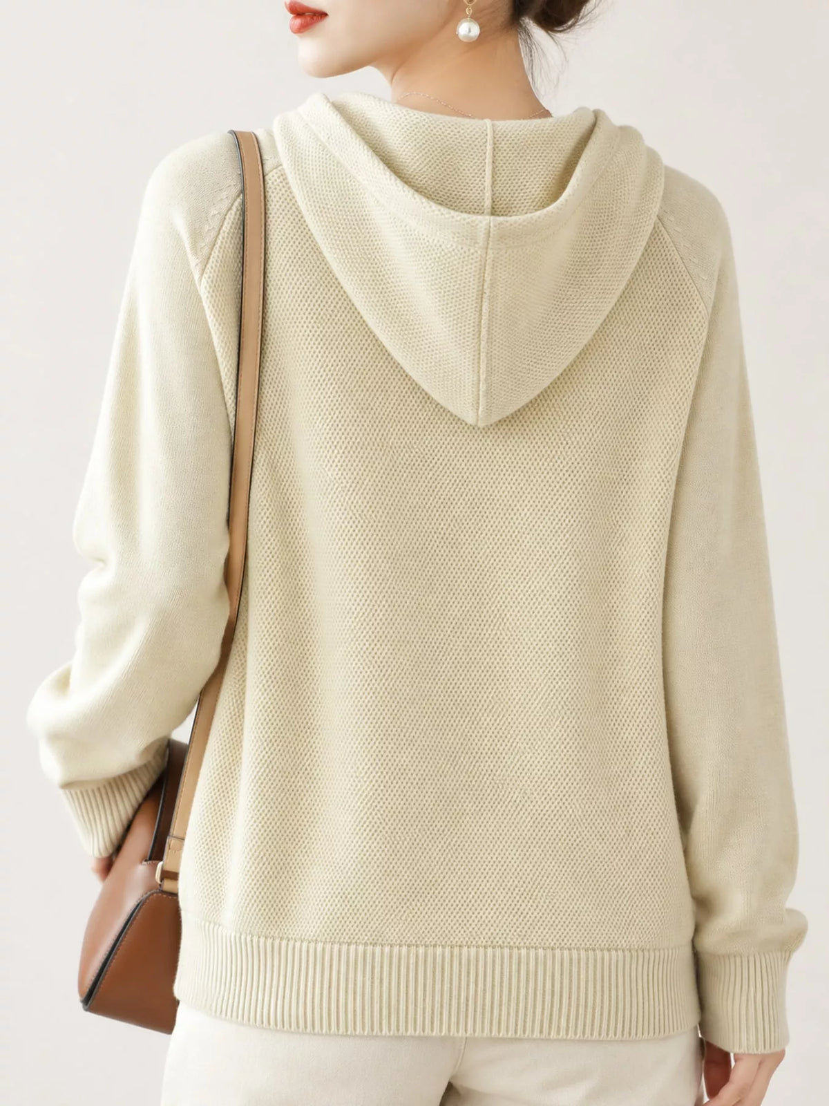 Back view of the cream knit sweater showing its hood and ribbed hem.