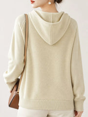 Back view of the cream knit sweater showing its hood and ribbed hem.