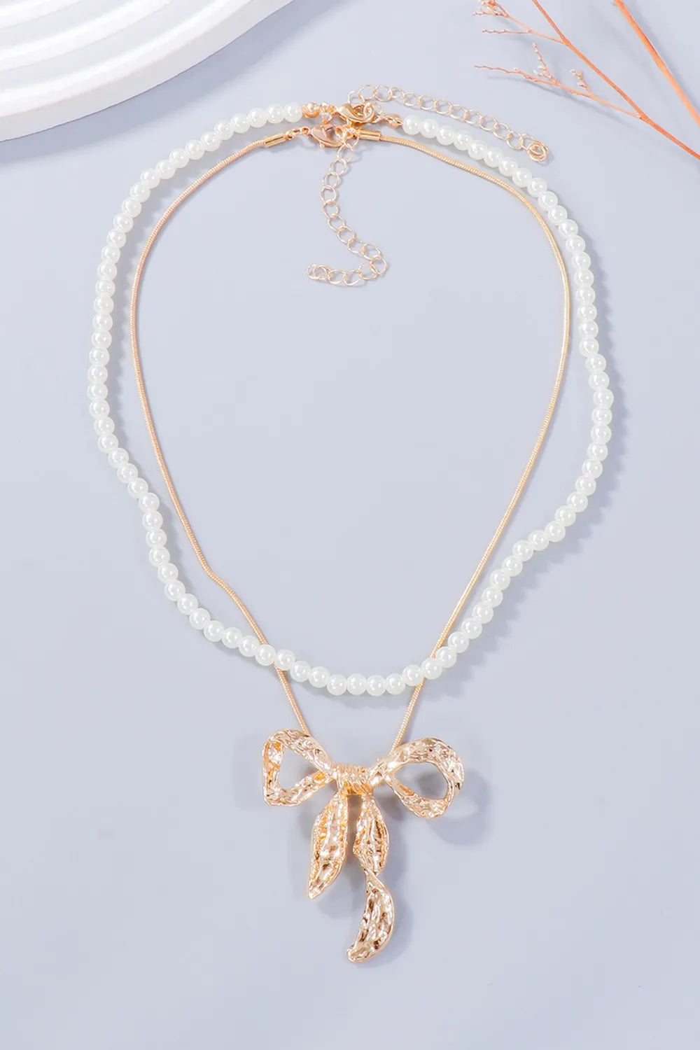 Full white beaded necklace with a gold-tone bow pendant and extension chain