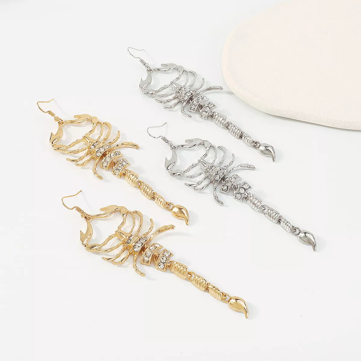Gold-tone and silver-tone scorpion earrings arranged diagonally