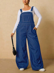 Medium blue overalls shown standing with one hand in a hip pocket and a small black bag.