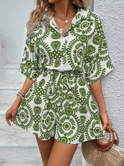 Women's green-and-white printed romper, front view holding woven handbag