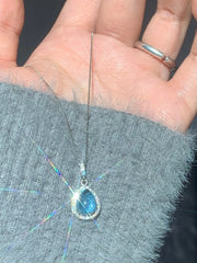 Blue crystal teardrop pendant held on a hand for scale