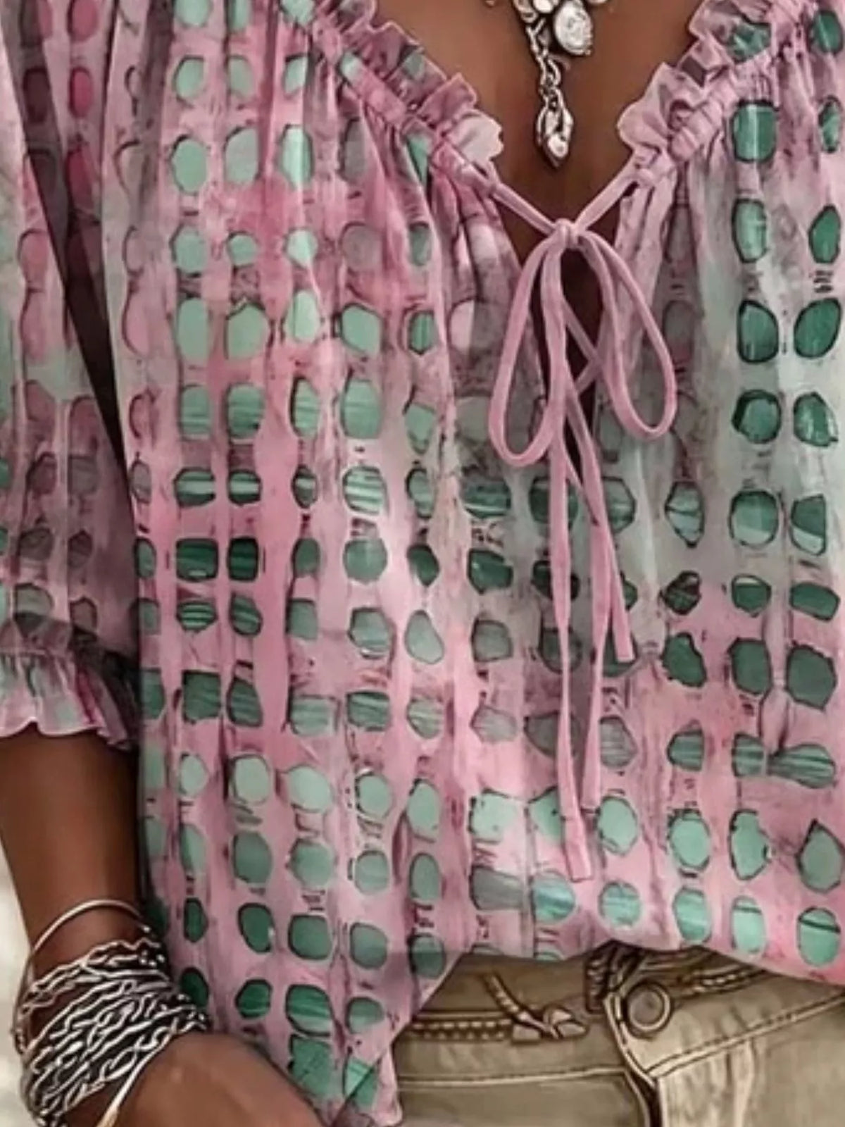 Close view of pink blouse with green spots, ruffled neckline and tied front