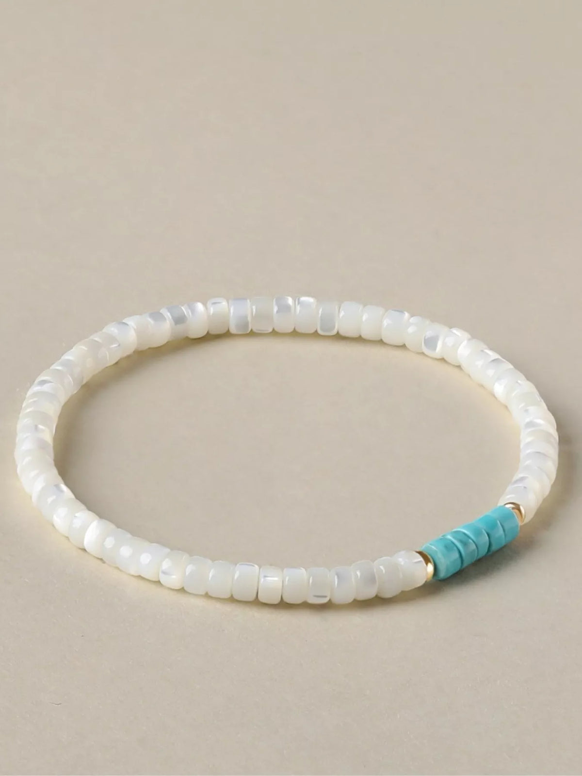 White rectangular beads form a bracelet with a turquoise bead section and gold-tone spacers