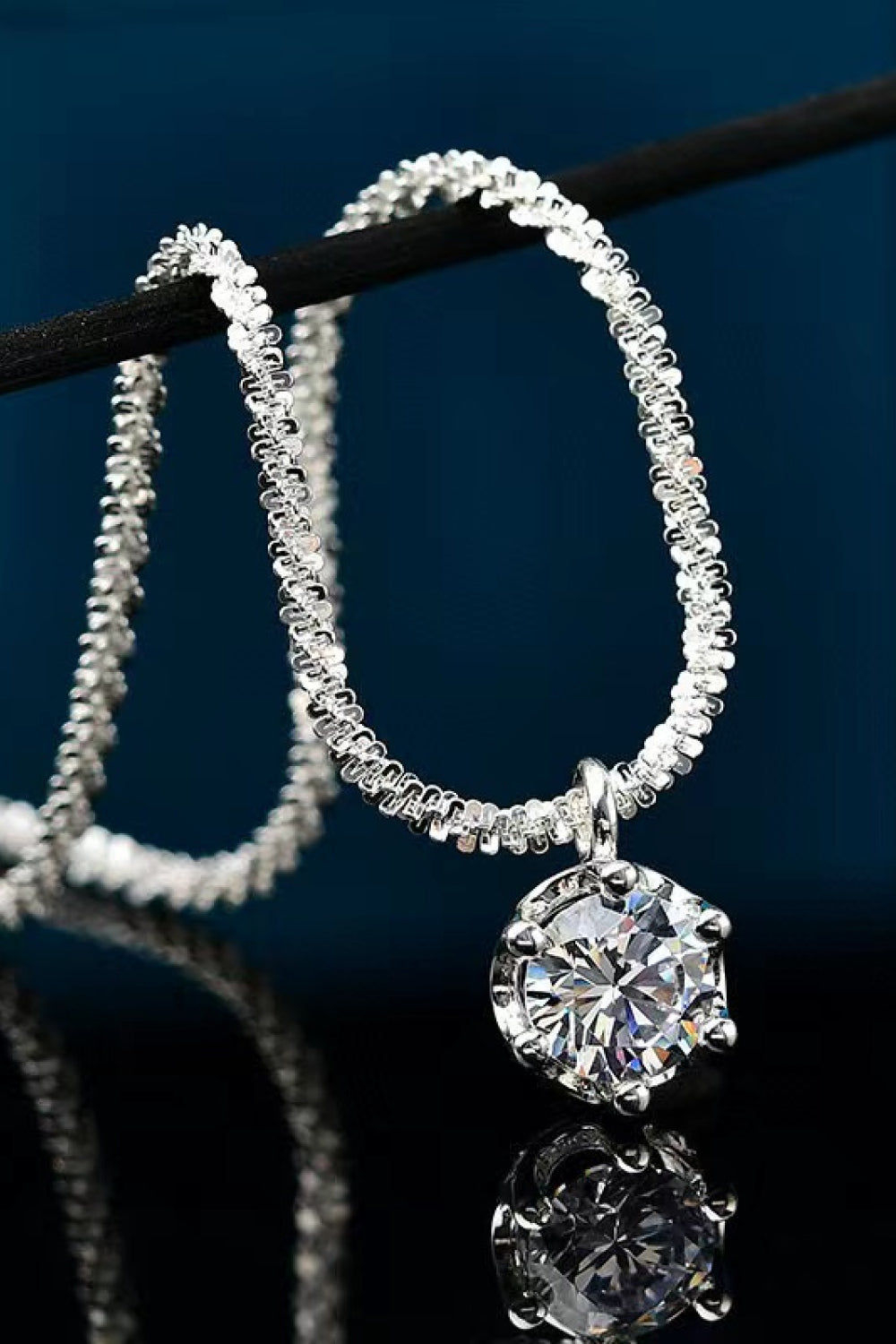 Round clear-stone pendant on a silver-tone chain looped over a dark display bar