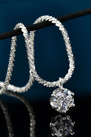 Round clear-stone pendant on a silver-tone chain looped over a dark display bar