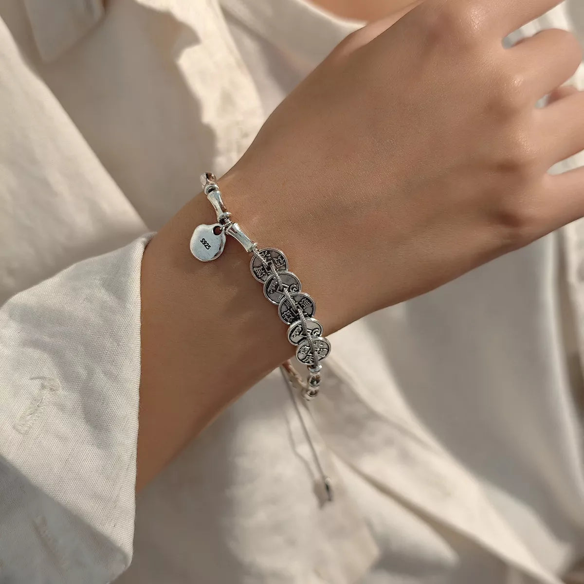 Silver-tone adjustable charm bracelet worn on a wrist above a white sleeve.