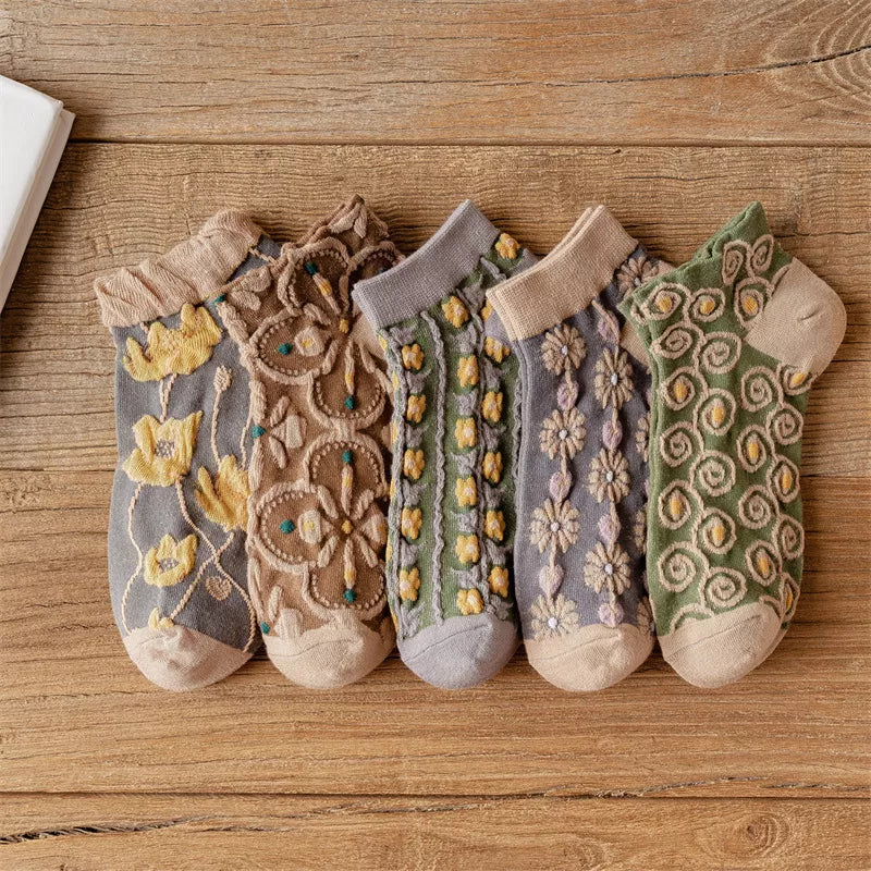 Five pairs of textured ankle socks with floral and spiral patterns laid on a wooden surface