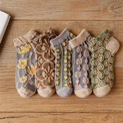 Five pairs of textured ankle socks with floral and spiral patterns laid on a wooden surface