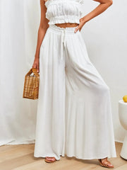 Model wearing white wide-leg pants with a woven bag