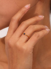 Gold-tone ring with a small blue round stone worn on finger