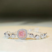 Angled view of a pink center stone with clear halo and round stones along the silver-tone chain
