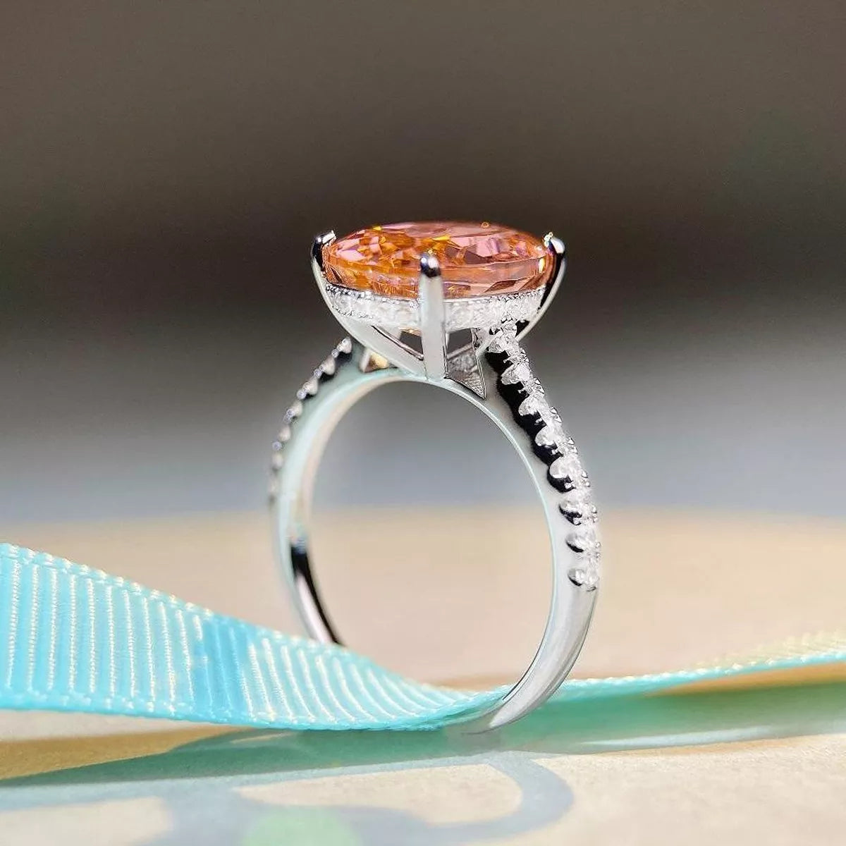 Side profile of a pink oval gemstone ring on a pale display surface