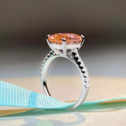 Side profile of a pink oval gemstone ring on a pale display surface