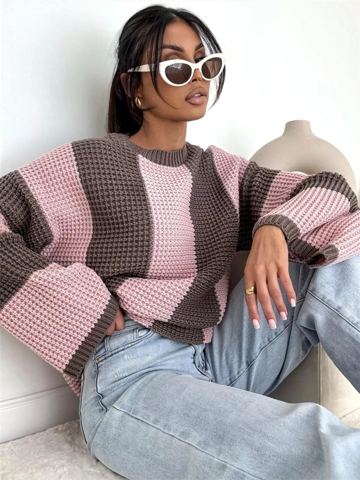 Seated model wearing pink and brown striped sweater and light jeans