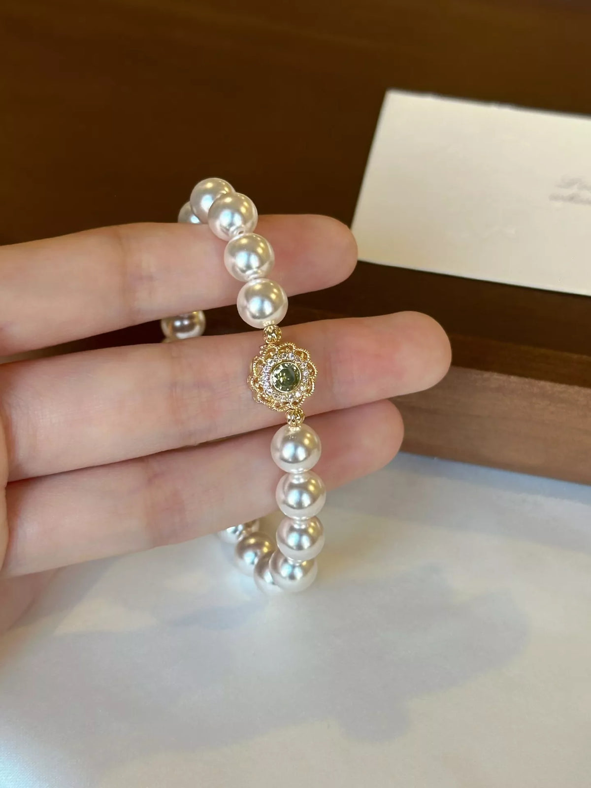 Close-up of round iridescent pearls and ornate green floral charm held in a hand