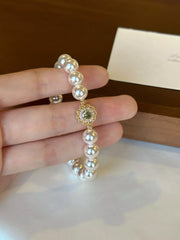 Close-up of round iridescent pearls and ornate green floral charm held in a hand