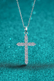 Clear-stone cross pendant on a silver-tone chain against teal fabric