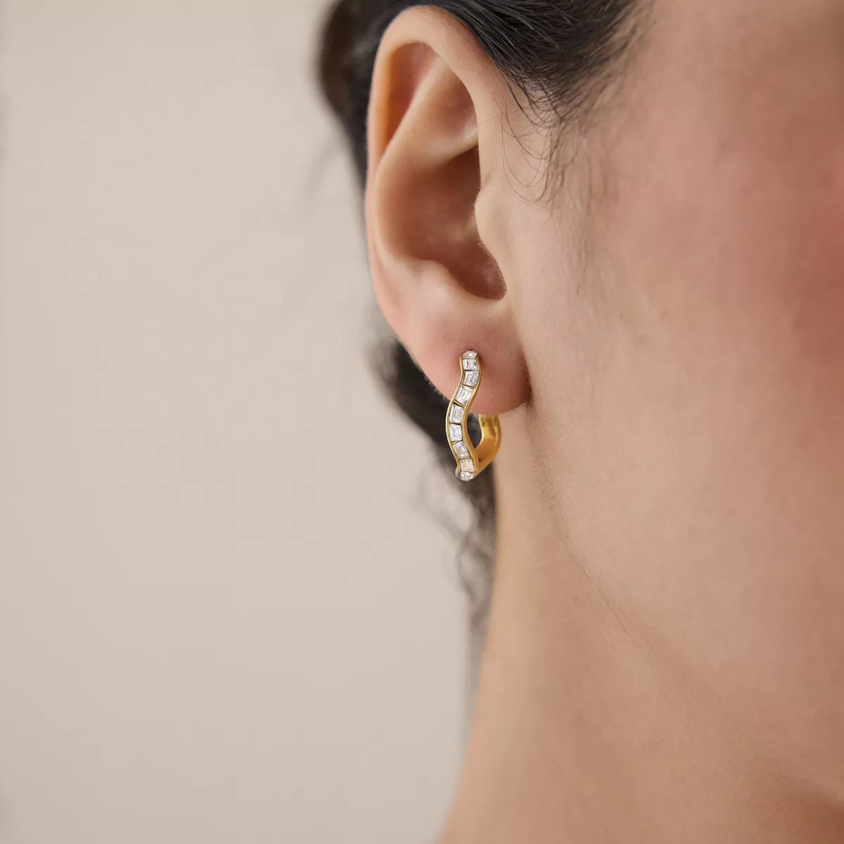 Close view of a gold-tone zircon hoop earring worn on an ear