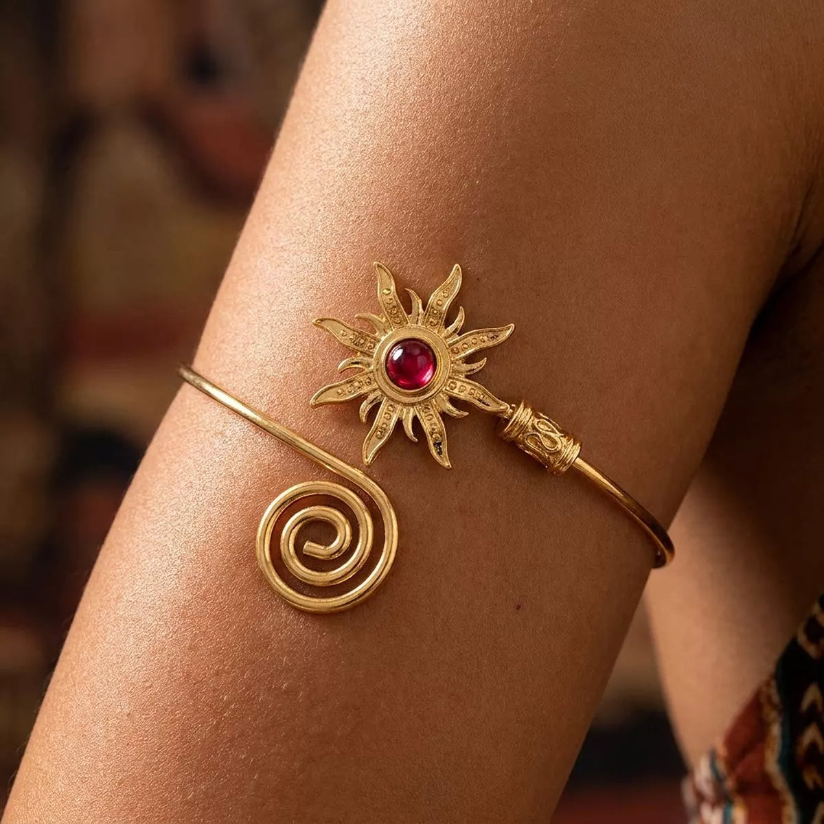 Gold-tone sunburst cuff bracelet with red center worn on a wrist