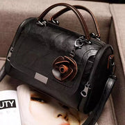 Black flap crossbody bag with brown flower ornament, viewed from the back and side