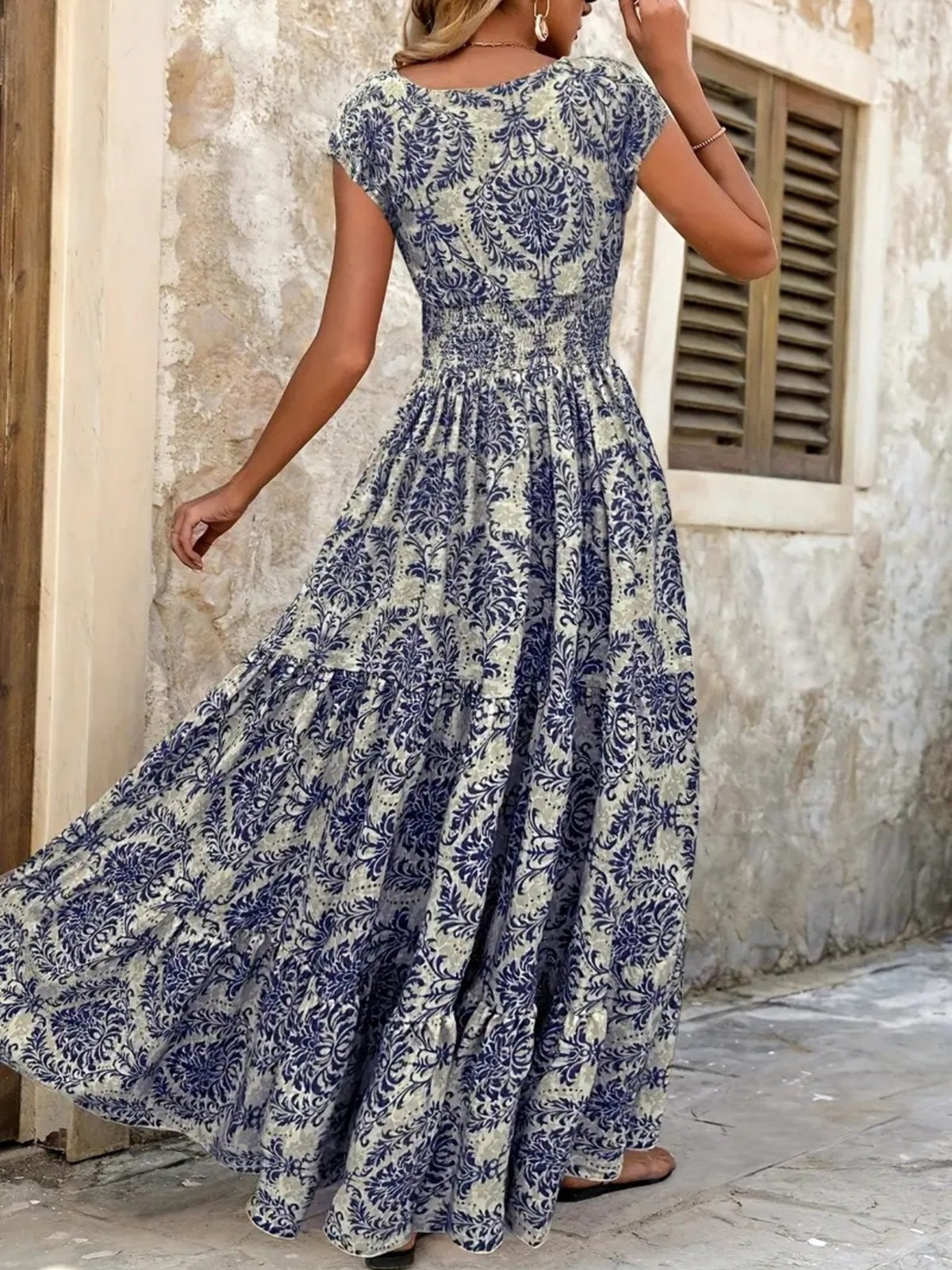 Back view of blue floral cap-sleeve maxi dress showing the smocked waist and flowing tiered skirt.