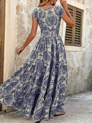 Back view of blue floral cap-sleeve maxi dress showing the smocked waist and flowing tiered skirt.